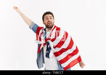 Ritratto di un entusiasta bello uomo barbuto indossando abiti casual in piedi isolato su sfondo bianco, indossa una bandiera americana Foto Stock