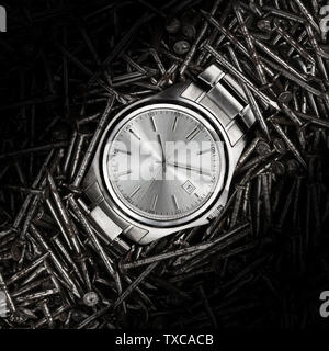 Una bella metallica in acciaio inox orologio da polso posa su un letto di costruzione metail chiodi closeup macro Foto Stock
