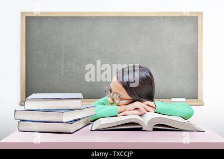 Asiatica ragazza carina con gli occhiali si addormenta sul libro sulla scrivania con sfondo lavagna Foto Stock