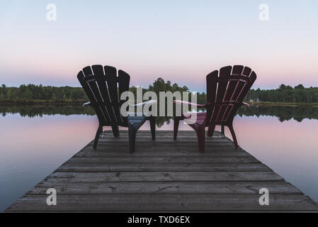 Due poltrone Adirondack seduti su un dock - Muskoka, Ontario, Canada. Foto Stock