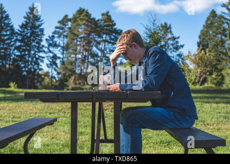 Interessato adolescente seduti ad un tavolo da picnic tutto solo con il suo telefono cellulare. Foto Stock