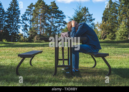 Interessato adolescente seduti ad un tavolo da picnic tutto solo con il suo telefono cellulare. Foto Stock