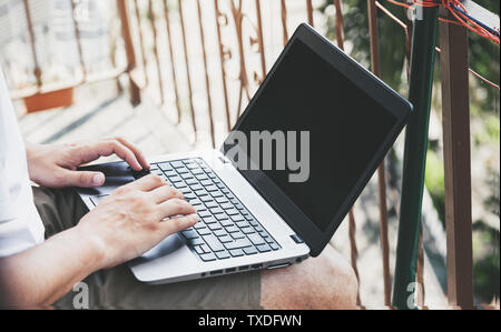 Uomo con notebook a casa sul suo balcone. Il lavoro creativo dello spazio. Il lavoro al di fuori il concetto di ufficio Foto Stock
