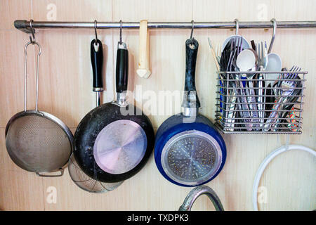 Utensili da cucina inclusi scolapasta, padella, pentola e alcuni argenti ex cucchiaio e forchetta sono appesi su rotaia nella dispensa parte della cucina. Foto Stock