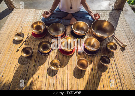 Donna che gioca su Tibetan Singing Bowl mentre è seduto sul materassino yoga contro una cascata. Tonned vintage. Bellissima ragazza con perle di mala meditando Foto Stock