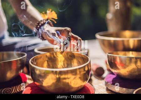 Donna che gioca su Tibetan Singing Bowl mentre è seduto sul materassino yoga contro una cascata. Tonned vintage. Bellissima ragazza con perle di mala meditando Foto Stock