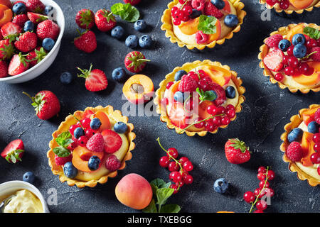 Close-up di estate tortine con crema di limone ripieno cremoso e rabboccato con lamponi, albicocche, mirtillo, fragola, ribes rosso e menta fresca su Foto Stock