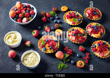 Estate pasticcini freschi con crema pasticcera ripieno cremoso e rabboccato con lamponi, albicocche, mirtillo, fragola, ribes rosso e menta fresca su un calcestruzzo Foto Stock