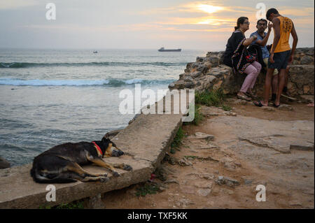 La gente seduta sulle pareti dei bastioni al tramonto sul bastione Flagrock, Galle, Sri Lanka Foto Stock