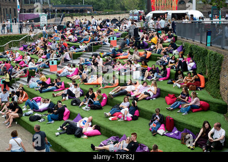 London, Kings Cross. Granary Square. Le persone a rilassarsi su erba artificiale passaggi coperti dal lato del Regent's Canal. Foto Stock