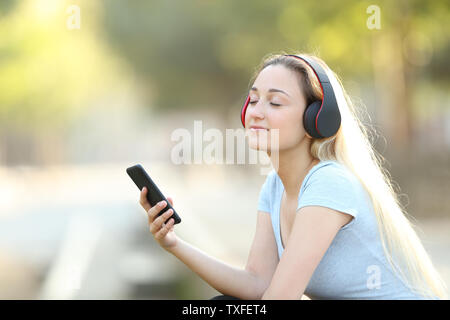 Ragazza adolescente ascoltando la musica con il telefono e le cuffie wireless rilassante in un parco Foto Stock