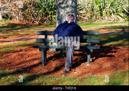 Un maschio adulto è di dormire su una panchina pubblica in un parco, ha la sua testa inclinata indietro Foto Stock
