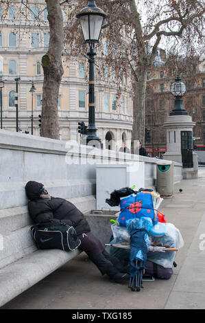 LONDON, Regno Unito - 25 gennaio 2011: senzatetto dorme su una panchina di pietra in Trafalgar Square Foto Stock