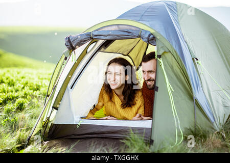 Giovane coppia adorabile in bright maglioni per godersi la natura, guardando fuori della tenda mentre si viaggia in alta montagna Foto Stock