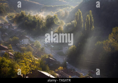 Vista aerea della bella foggy villaggio tra le montagne di Lovech, Bulgaria. Misty sunrise vista del quartiere della città circondata da rocce della montagna. Sun bea Foto Stock