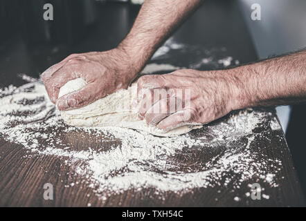 Close-up di mani di uomo impastare la pasta lievitata su infarinato e contatore di cucina Foto Stock