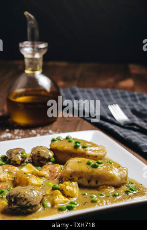 Foto verticale di sano spagnolo tradizionale piatto di nasello verde con salsa di frutti di mare con vongole, gamberi e piselli verdi e uovo, tipica cucina mediterranea Foto Stock