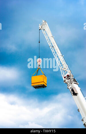 Braccio della gru con gancio di sollevamento di un contenitore giallo in porto contro il cielo blu. Foto Stock
