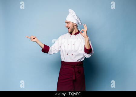 Professional positivo uomo felice chef mostra una gustosa ok segno isolato su luce blu. Foto Stock