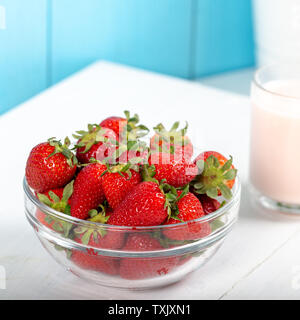 Fragole fresche in una ciotola di vetro e un bicchiere di latte alla fragola Foto Stock