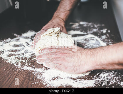 Close-up di mani di uomo impastare la pasta lievitata su infarinato e contatore di cucina Foto Stock