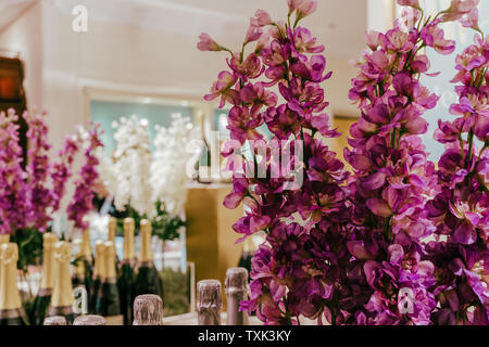 Bouquet di fiori viola a fuoco con bottiglie di champagne in fondo al di fuori della messa a fuoco. Foto Stock