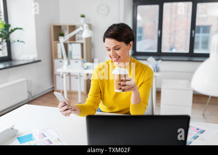 Donna felice con caffè utilizza lo smartphone in ufficio Foto Stock