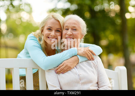 Figlia di madre senior avvolgente su una panchina nel parco Foto Stock