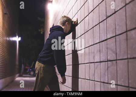 Sconvolto adolescente appoggiata contro un muro di mattoni in un vicoletto. Egli soffre di depressione. Foto Stock
