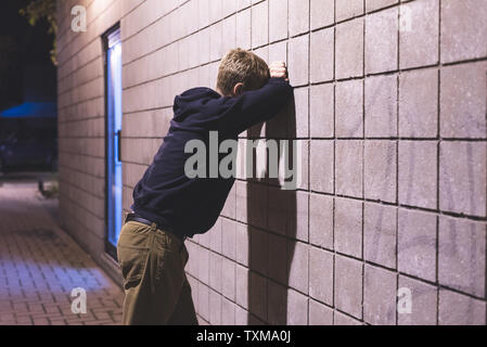 Sconvolto adolescente appoggiata contro un muro di mattoni in un vicoletto. Egli soffre di depressione. Foto Stock