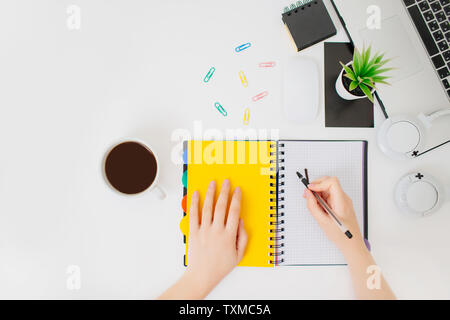 Donna workplace, mani femminili la scrittura in un blocco note. Flatlay con le mani, macbook, tazza da caffè, le cuffie e il blocco note. Foto Stock