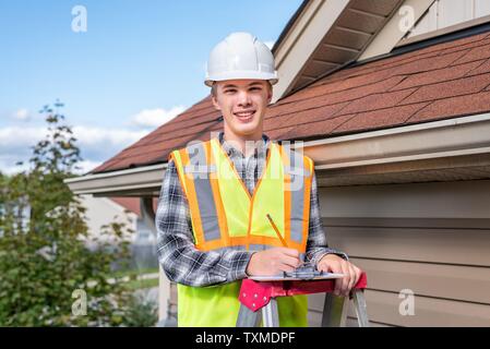 Home inspector in piedi su una scaletta e fornendo una ispezione al tetto di una casa. Foto Stock