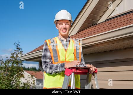 Home inspector in piedi su una scaletta e fornendo una ispezione al tetto di una casa. Foto Stock