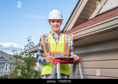 Home inspector in piedi su una scaletta e fornendo una ispezione al tetto di una casa. Foto Stock