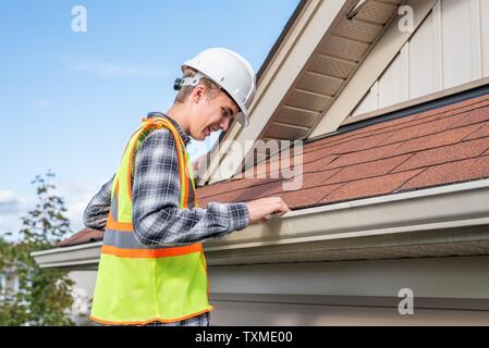 Home inspector in piedi su una scaletta e fornendo una ispezione al tetto di una casa. Foto Stock