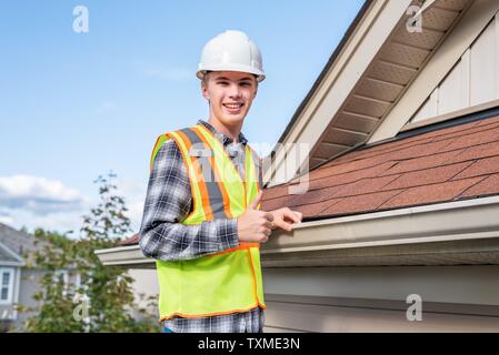 Home inspector in piedi su una scaletta e fornendo una ispezione al tetto di una casa. Foto Stock