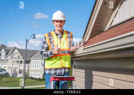 Home inspector in piedi su una scaletta e fornendo una ispezione al tetto di una casa. Foto Stock