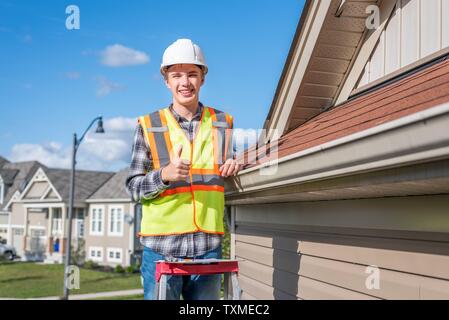 Home inspector in piedi su una scaletta e fornendo una ispezione al tetto di una casa. Foto Stock