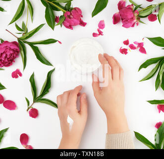 Due mani femminili e un vaso con crema pasticcera e borgogna peonie fiorite con foglie verdi, concetto di anti-invecchiamento delle procedure per il ringiovanimento e mo Foto Stock