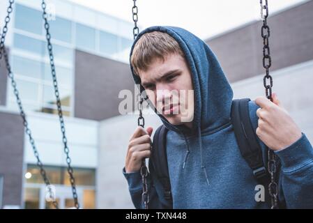 Triste adolescente seduto su una oscillazione al di fuori di una scuola. Egli è ricordando quando era più giovane. Foto Stock