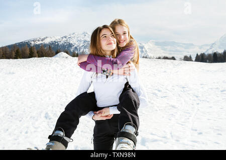 Ragazza adolescente sciatore getting piggyback dal miglior amico in paesaggi innevati, ritratto, Tirolo, Stiria, Austria Foto Stock