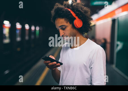 Giovane uomo utilizza lo smartphone sulla piattaforma del treno Foto Stock