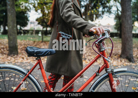 Giovane donna spingendo in bicicletta in autunno park, il collo verso il basso Foto Stock