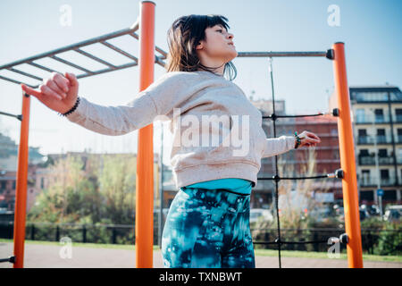 Classe Calisthenics presso palestra all'aperto, giovane donna salta con le braccia aperte Foto Stock