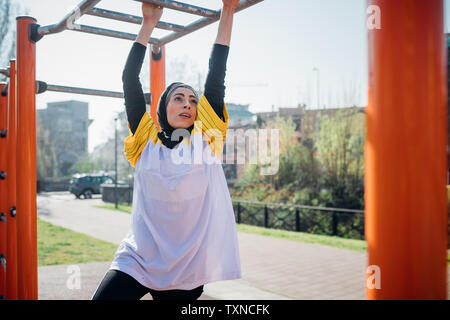 Classe Calisthenics presso palestra all'aperto, giovane donna pendenti da attrezzatura ginnica Foto Stock