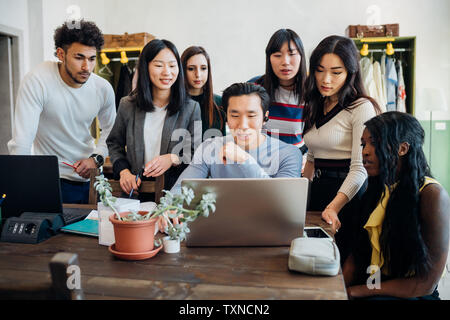 Un gruppo di giovani uomini e donne d'affari guardando il laptop in office meeting Foto Stock