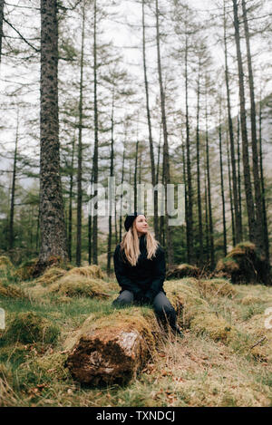 Donna seduta su log, Trossachs National Park, Canada Foto Stock