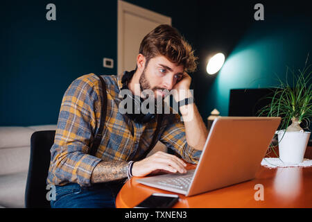 Metà uomo adulto seduto al tavolino da soggiorno guardando al laptop Foto Stock