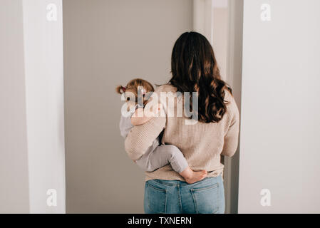 Madre bambino portando la figlia attraverso la hall porta, vista posteriore Foto Stock