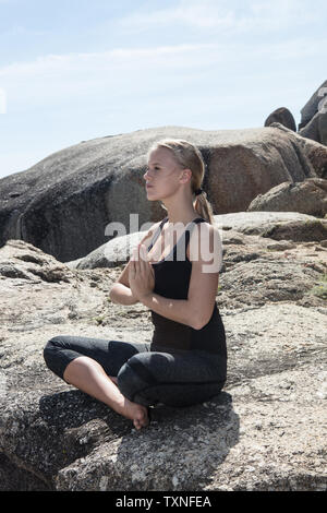 Giovane donna pratica lotus yoga pone sulla spiaggia rock, Cape Town, Western Cape, Sud Africa Foto Stock